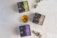 Three square boxes labeled with herbal tea names lie on a light textured surface. A glass cup filled with tea, containing a tea bag, is placed near the center. Two eucalyptus branches extend into the scene from the edges.