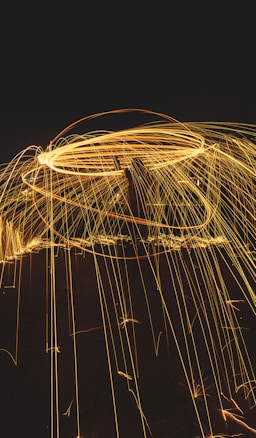 Bright sparks create circular and linear patterns against a dark background, suggestive of long-exposure photography with moving lights.