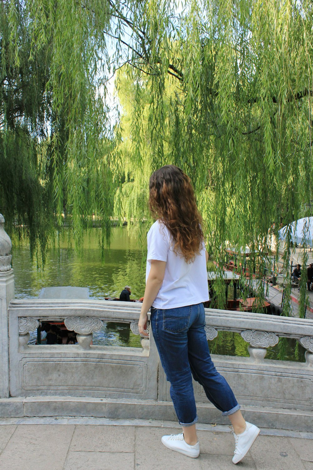 woman in white t-shirt and blue denim jeans standing on gray concrete dock during daytime