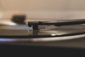 A close-up view of a vinyl record player with the needle arm resting on the spinning disc. The focus is on the stylus and the grooves of the record, suggesting an appreciation for analog music.