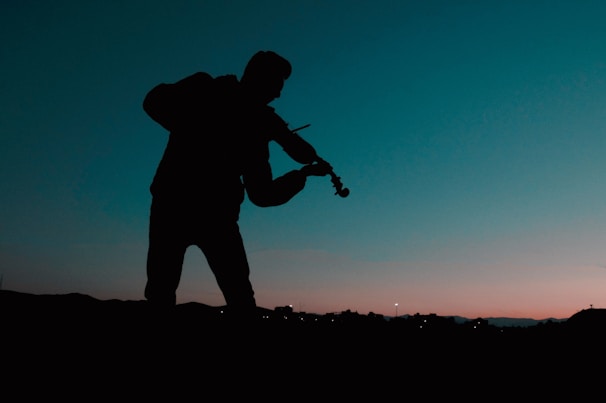A sunset silhouette of the cellist playing on a garden terrace, with twinkling fairy lights overhead.