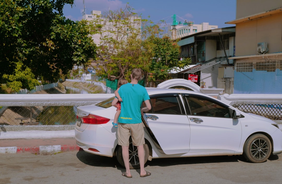 man in blue polo shirt standing beside white sedan during daytime