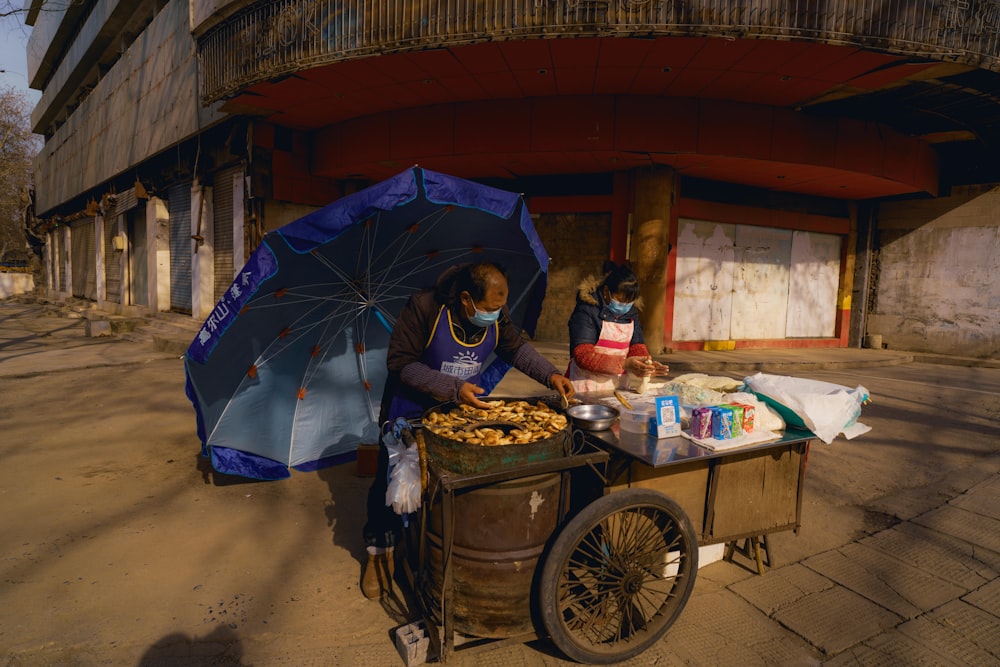 man in black jacket holding umbrella standing beside brown wooden cart