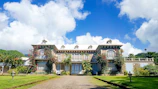 A majestic large luxury home with tropical landscaping and a clear blue sky backdrop.