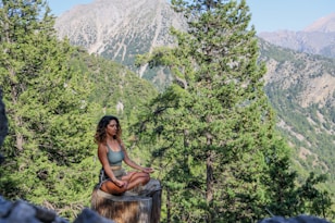woman in black tank top sitting on brown wooden log during daytime