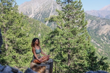 woman in black tank top sitting on brown wooden log during daytime