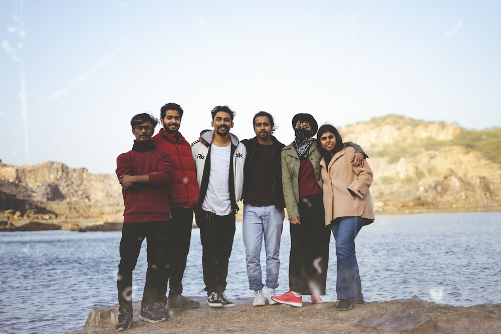 4 men standing on brown rock near body of water during daytime