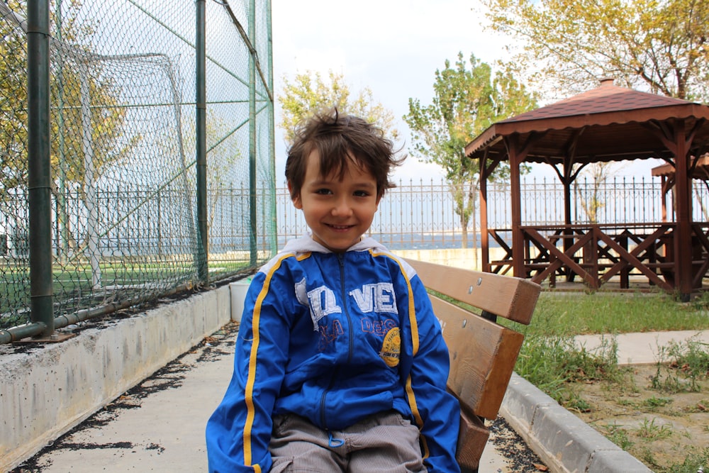 boy in blue and yellow jacket sitting on brown wooden bench
