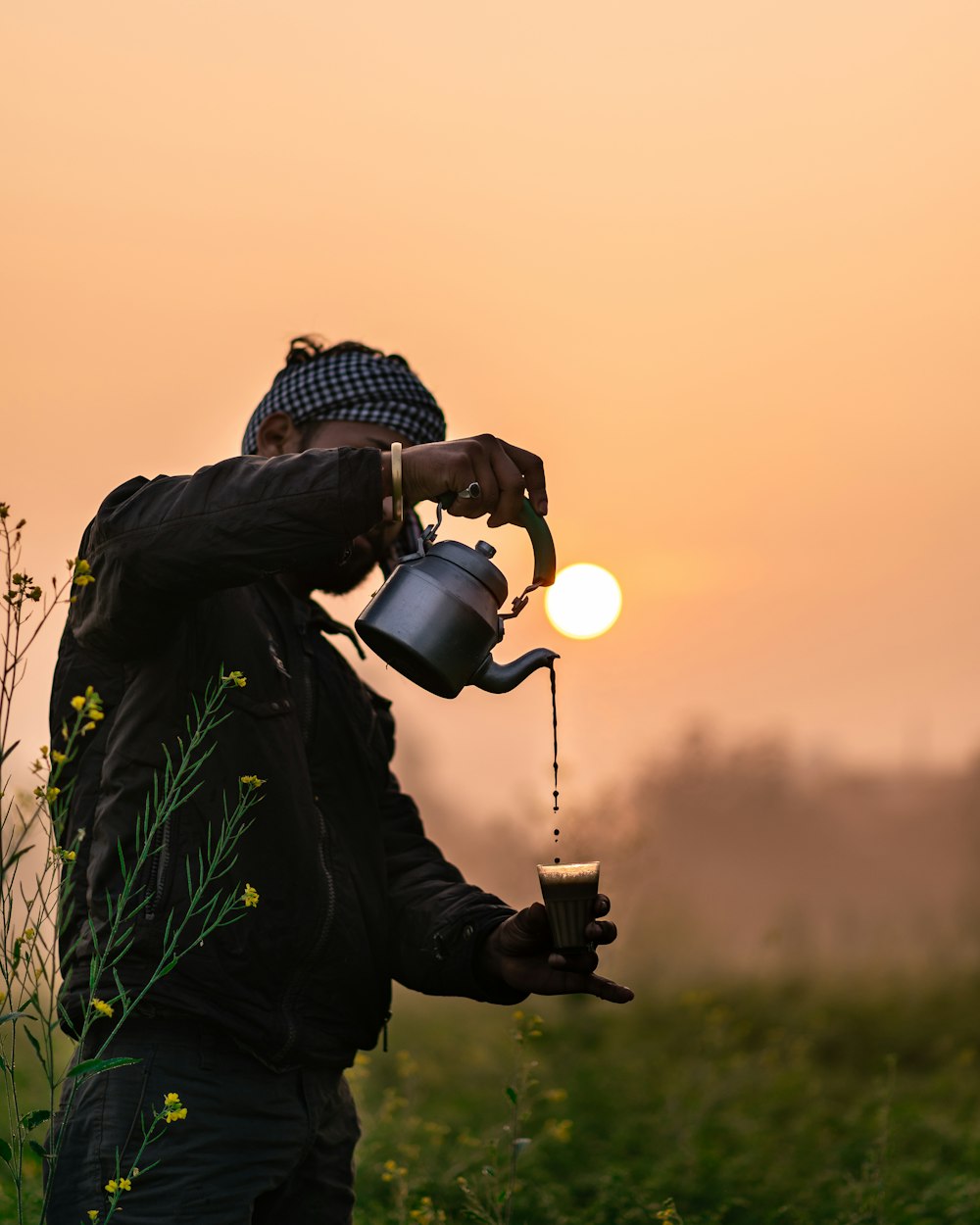 a man standing in a field drinking from a coffee pot