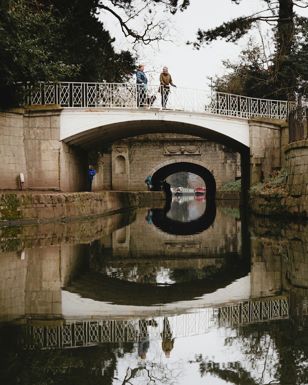 man in white t-shirt and blue denim jeans standing on brown concrete bridge during daytime