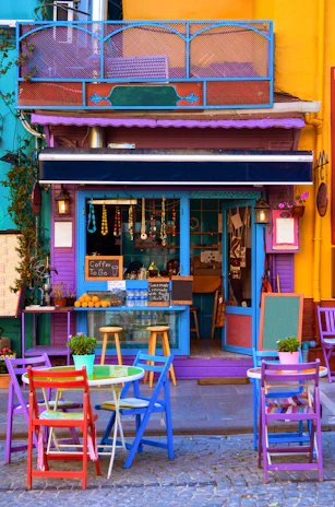 A lively street-side coffee shop with colorful signage framed by tropical plants.