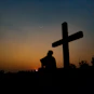 silhouette of man standing near cross during sunset
