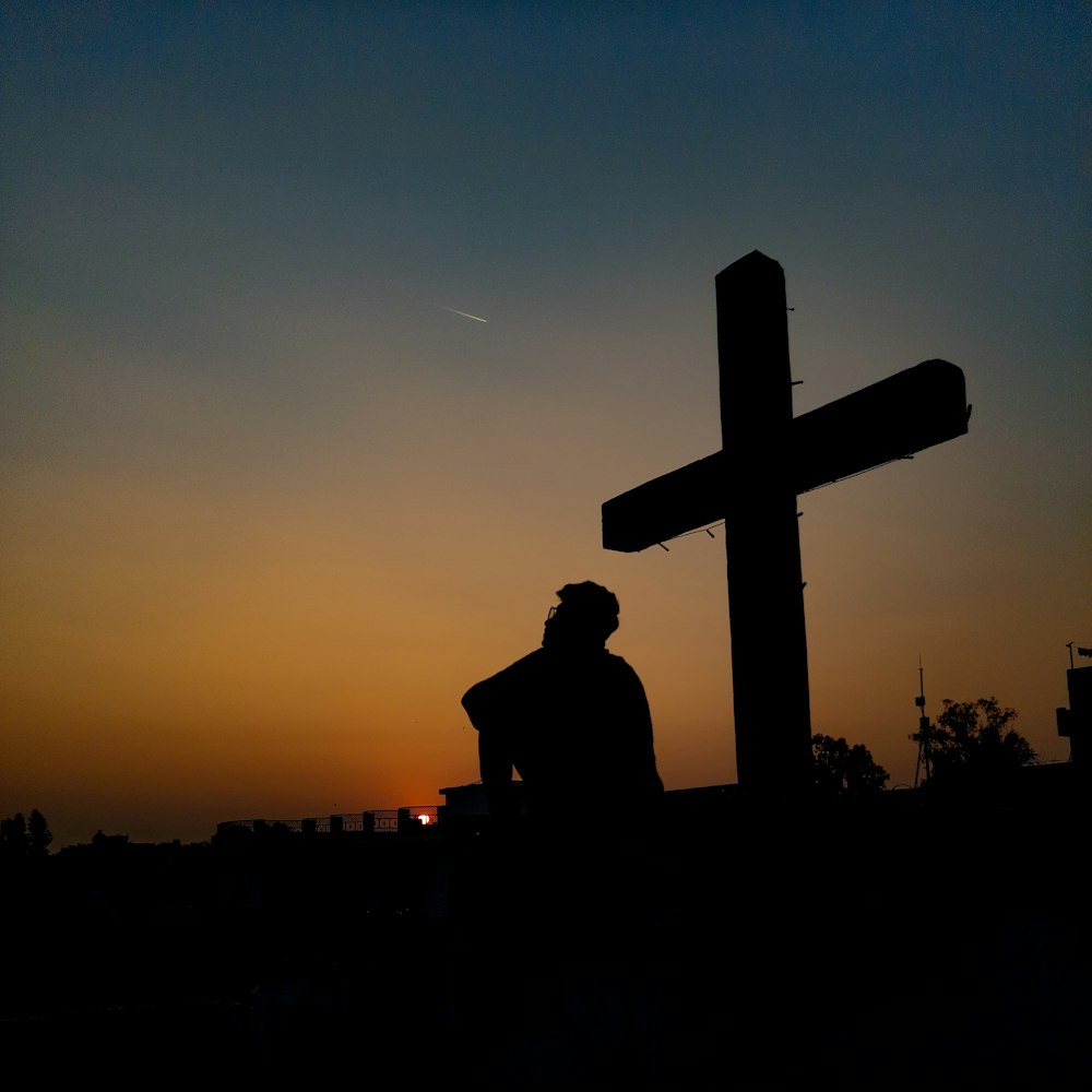 silhouette of man standing near cross during sunset
