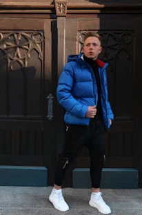 man in blue jacket standing near black wooden door