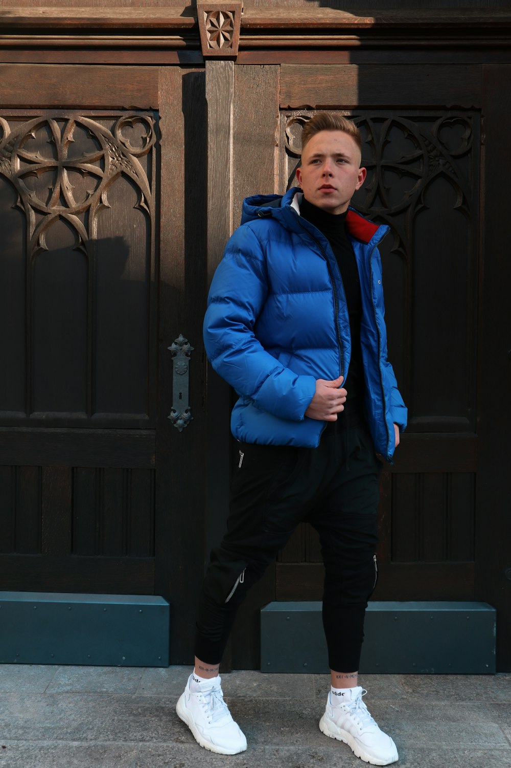 man in blue jacket standing near black wooden door