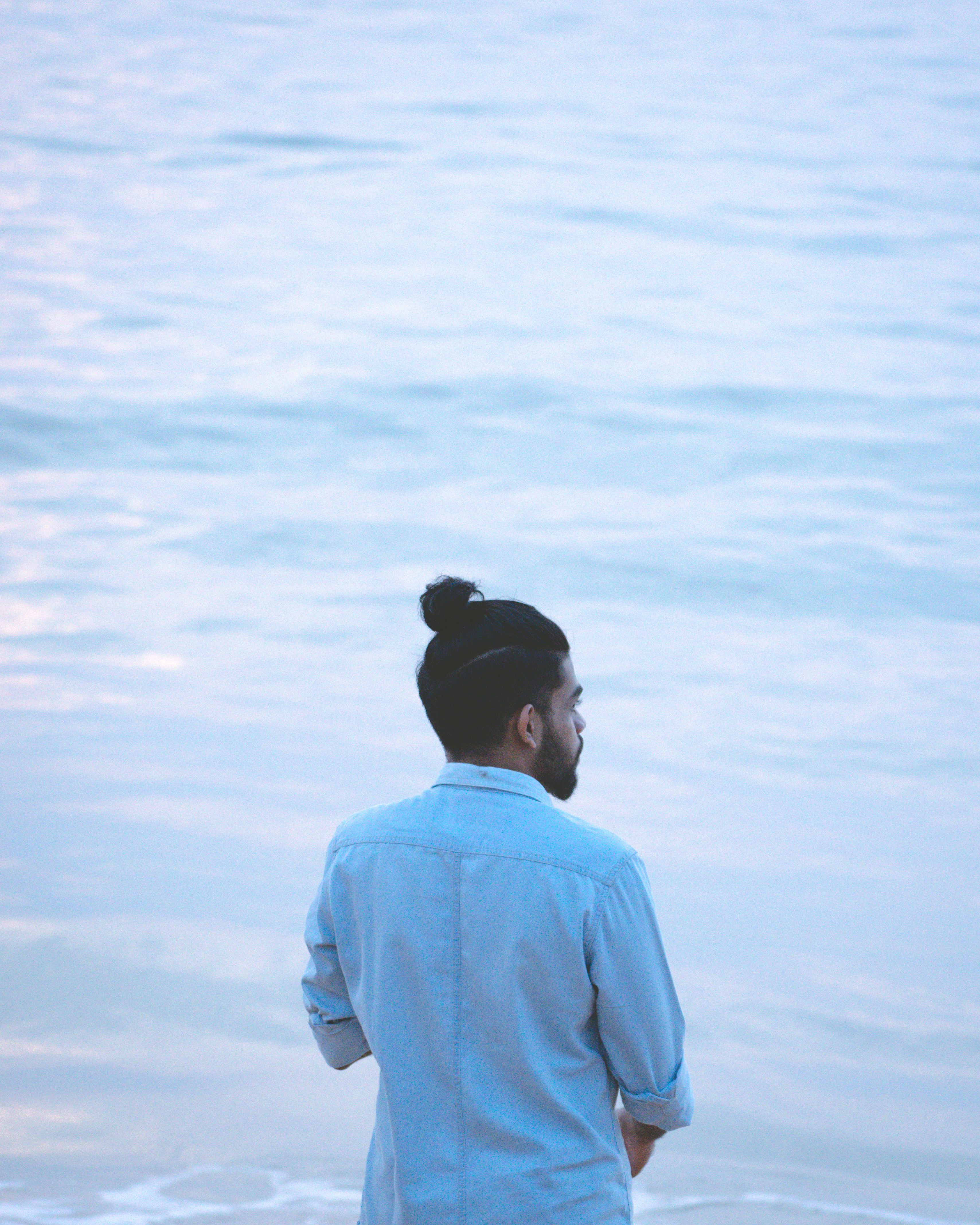 man in blue dress shirt and black hat standing in front of white clouds during daytime