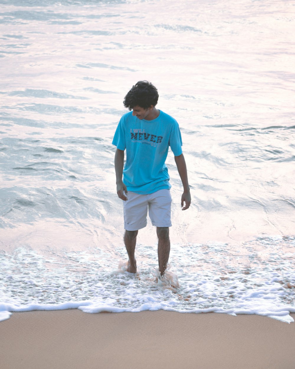 man in red crew neck t-shirt and white shorts standing on seashore during daytime