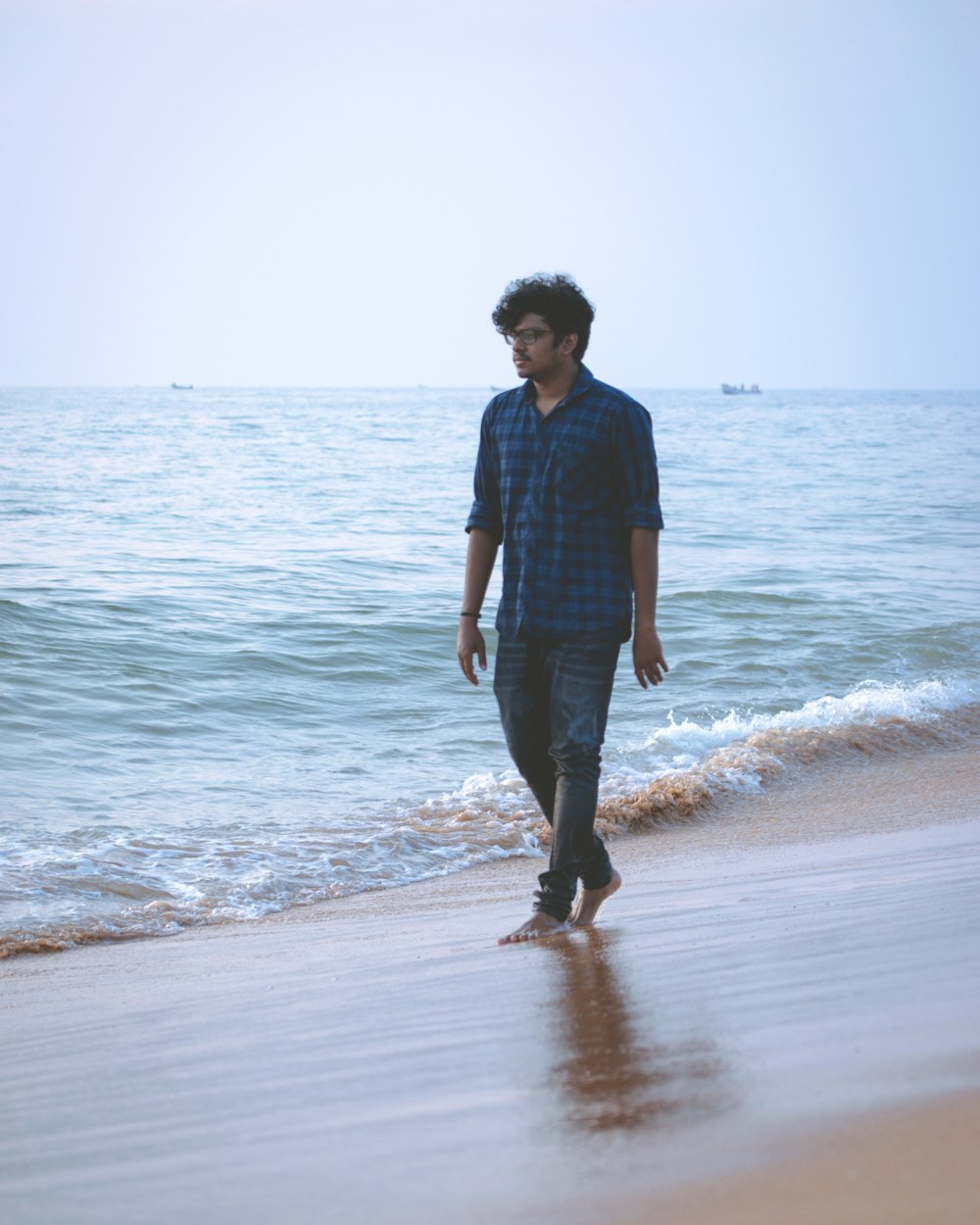 man in black dress shirt and blue denim jeans standing on seashore during daytime