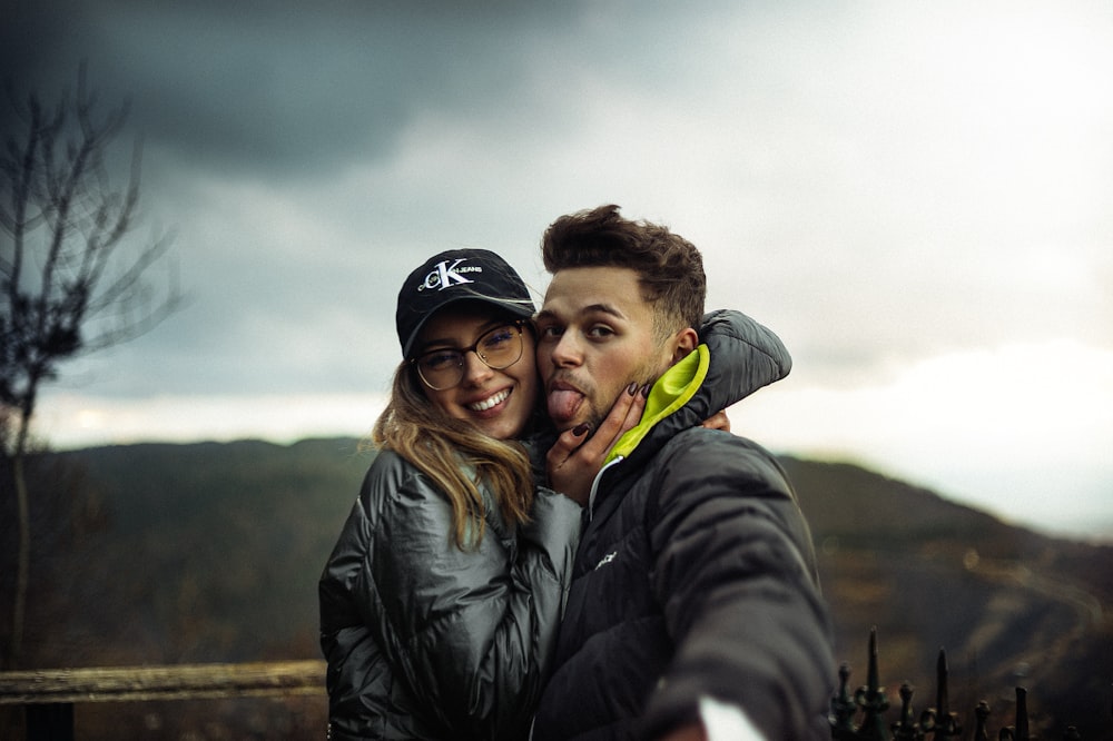 man in black jacket hugging woman in green scarf