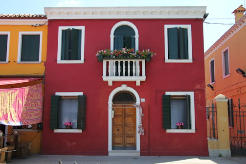 Before and after photos of a freshly painted Alicante building exterior with vibrant crimson and forest green accents