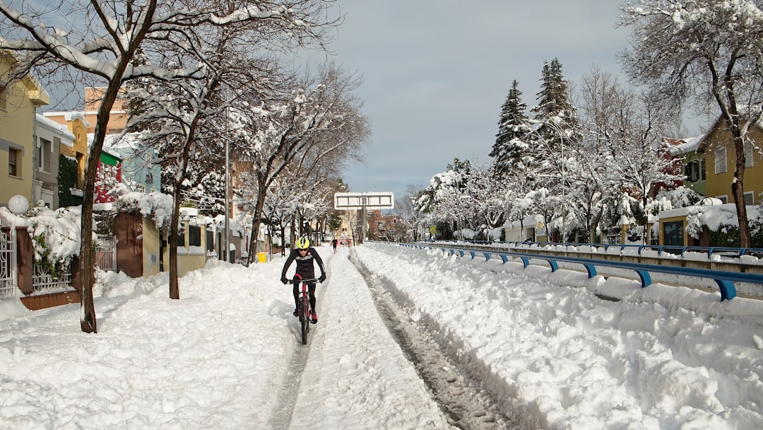 person in black jacket riding bicycle on snow covered road during daytime