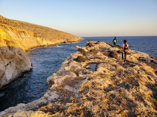 2 men standing on brown rock formation near body of water during daytime in Qrendi Malta