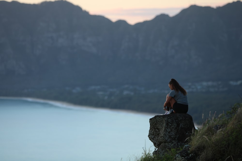 woman in black tank top sitting on rock near body of water during daytime