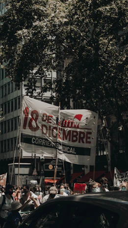 A vibrant street protest in Guanajuato with people holding red and black banners under a cloudy sky.