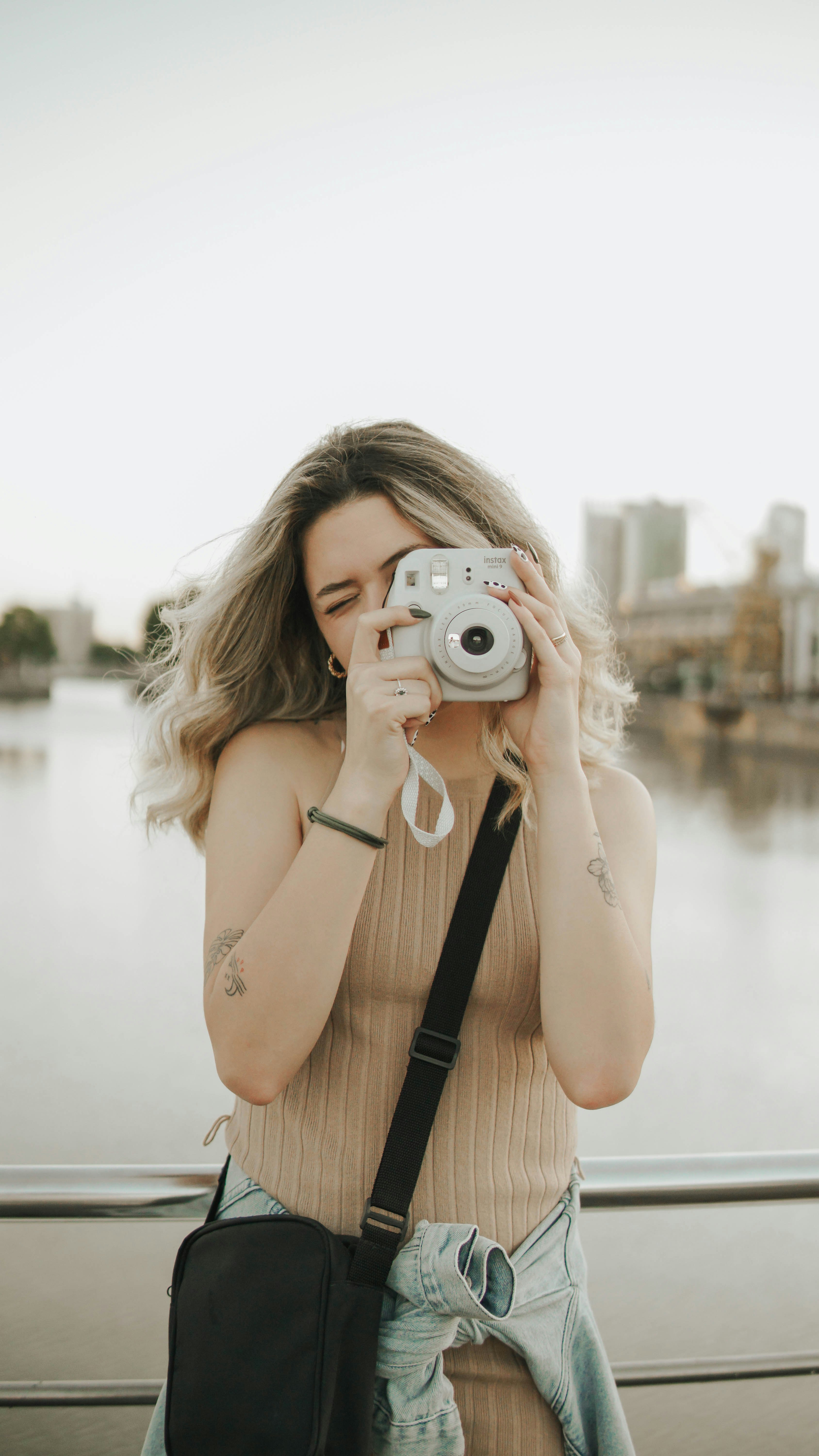 woman in black tank top holding silver point and shoot camera