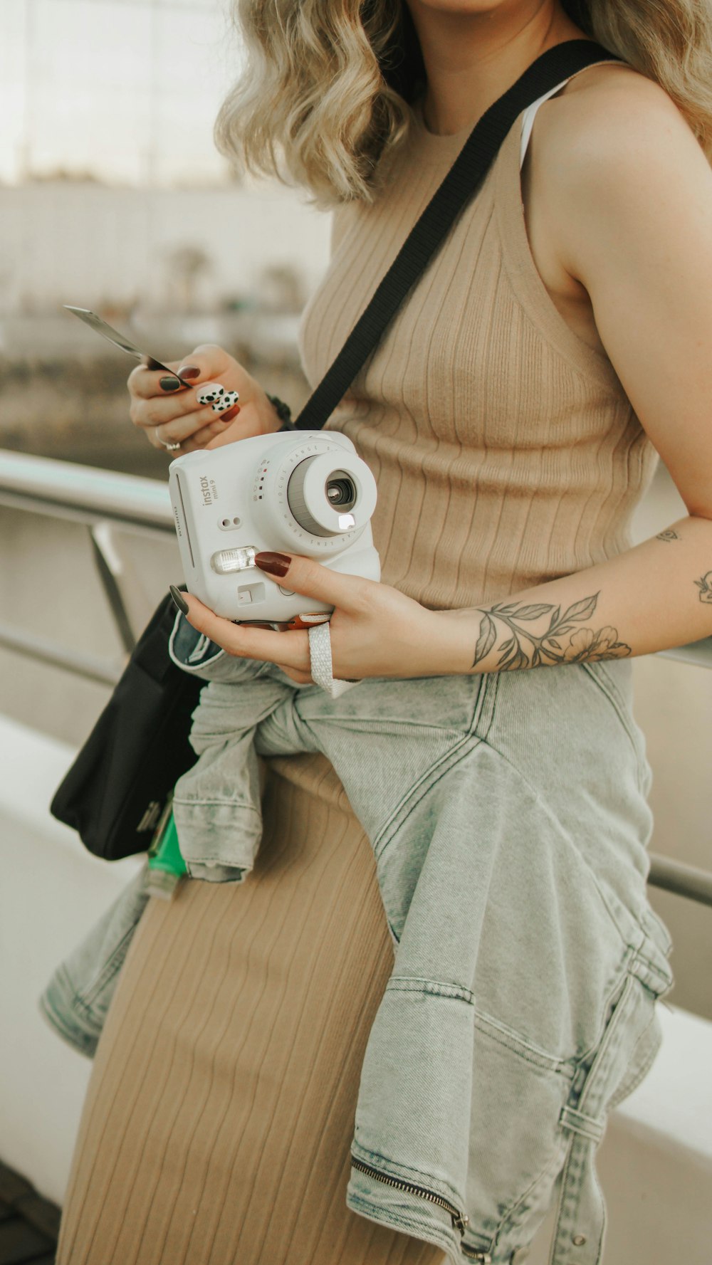 woman in brown tank top and gray denim shorts holding white point and shoot camera