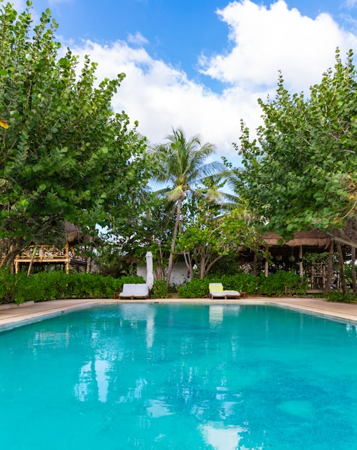Inviting pool area surrounded by lush greenery and comfortable lounge chairs under blue skies
