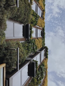 A vertical garden covers the facade of a building with lush greenery and various plant species arranged in a pattern alongside window panels. The sky is visible, featuring scattered clouds.