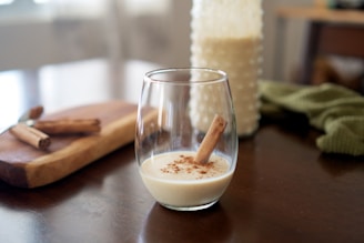 Close-up of a creamy glass of Haitian kremas with a sprinkle of nutmeg and a cinnamon stick garnish.