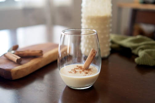 Close-up of a creamy glass of Haitian kremas with a sprinkle of nutmeg and a cinnamon stick garnish.