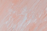 The image features a close-up of thick, textured brushstrokes in varying shades of pale peach and white, creating an abstract pattern. The brushwork appears dynamic, with a mixture of smooth and rugged textures, adding depth to the visual composition.