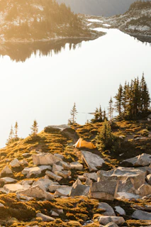 A rugged tent pitched beside a serene mountain lake at sunrise