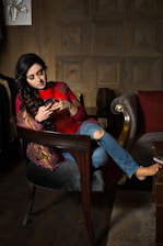 woman in red and white long sleeve shirt sitting on brown wooden armchair