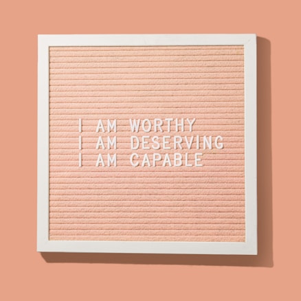 A peach-colored letter board framed in white displays motivational phrases in white letters: 'I AM WORTHY', 'I AM DESERVING', 'I AM CAPABLE'.