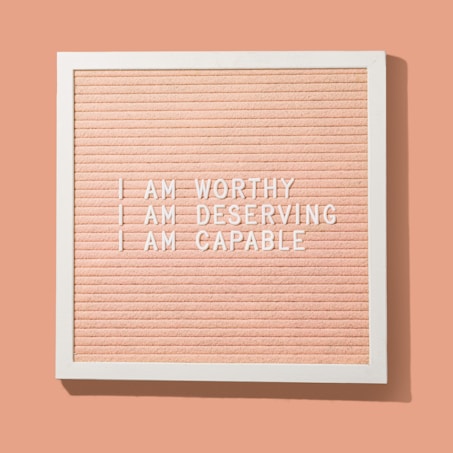 A peach-colored letter board framed in white displays motivational phrases in white letters: 'I AM WORTHY', 'I AM DESERVING', 'I AM CAPABLE'.