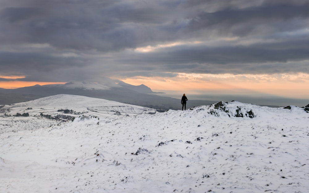 person walking on snow covered field during sunset