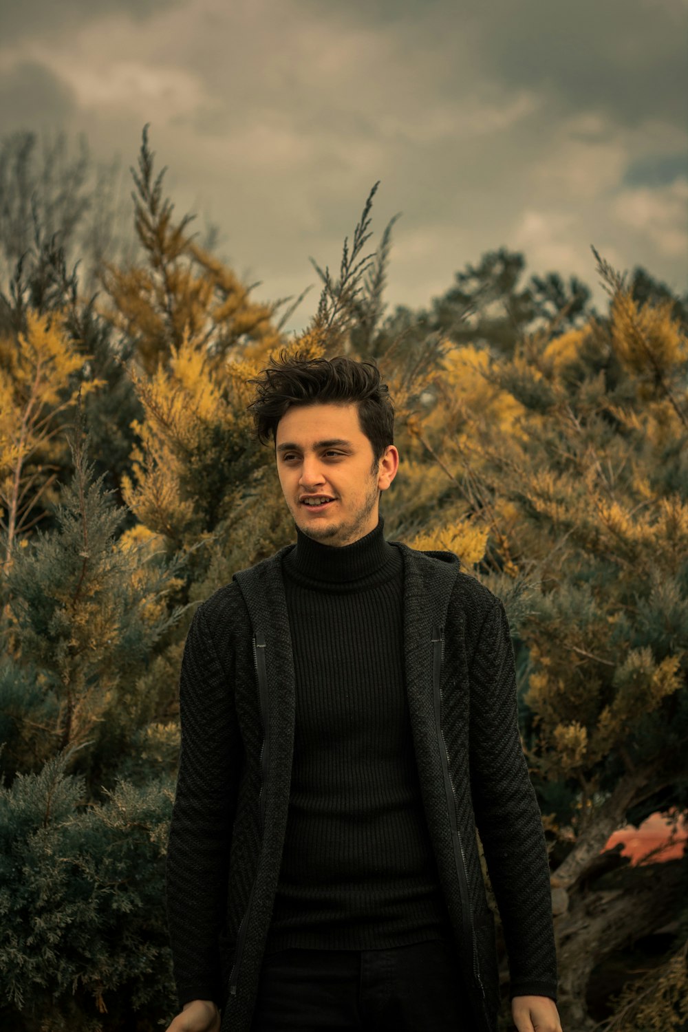 man in black turtleneck sweater standing near brown trees during daytime