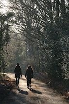 2 person walking on pathway between trees during daytime