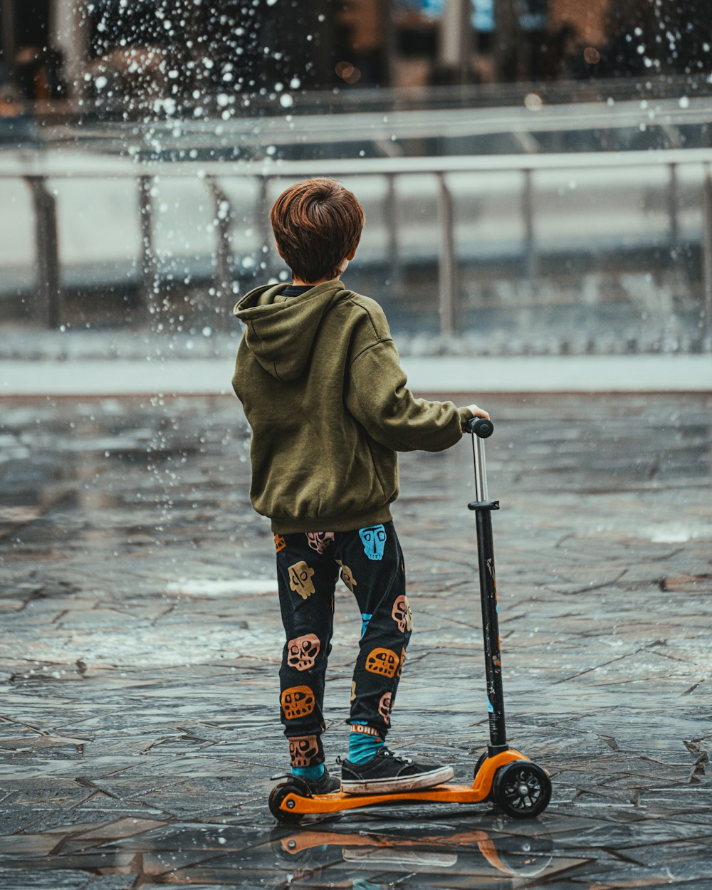 child in brown hoodie and blue pants standing on gray concrete floor
