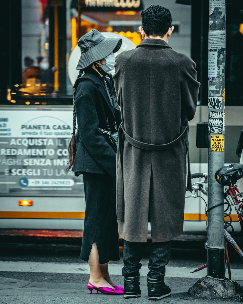 uomo in cappotto nero e cappello marrone in piedi sul marciapiede durante il giorno