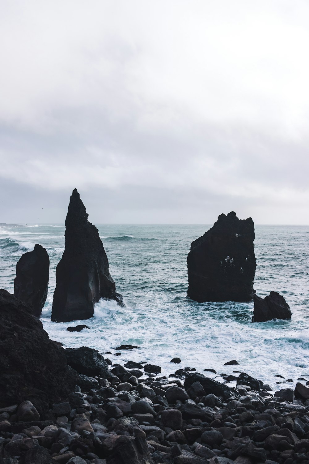 black rock formation on sea under white clouds during daytime