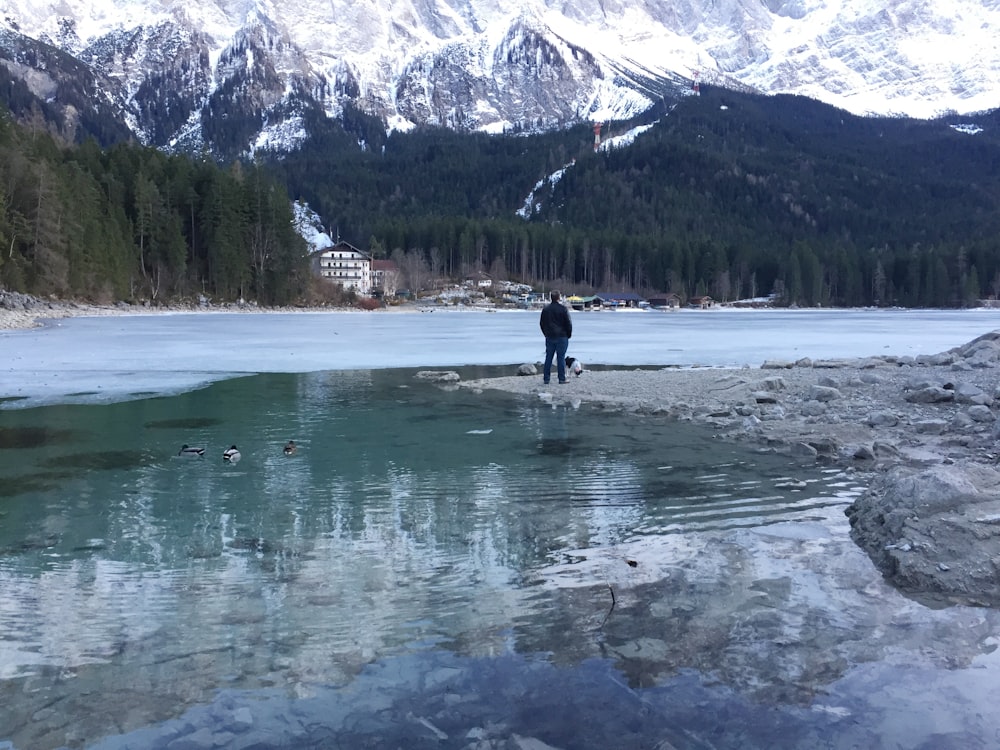 person in black jacket and pants walking on wet sand near body of water during daytime