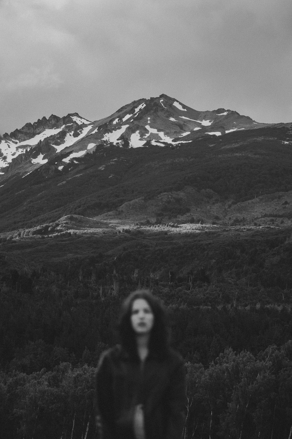 grayscale photo of woman standing on grass field near mountain