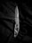 A silver folding knife is placed on a dark, textured fabric. The knife features an intricate cutout design on its handle and has a sharp, polished blade with a serrated edge near the base.