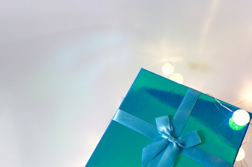 A shiny blue gift box with a matching ribbon is partially visible. The background is light with several glowing white lights creating a cozy ambiance.