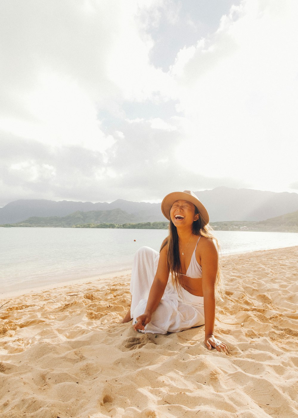 woman in white tank top and white hat sitting on beach during daytime